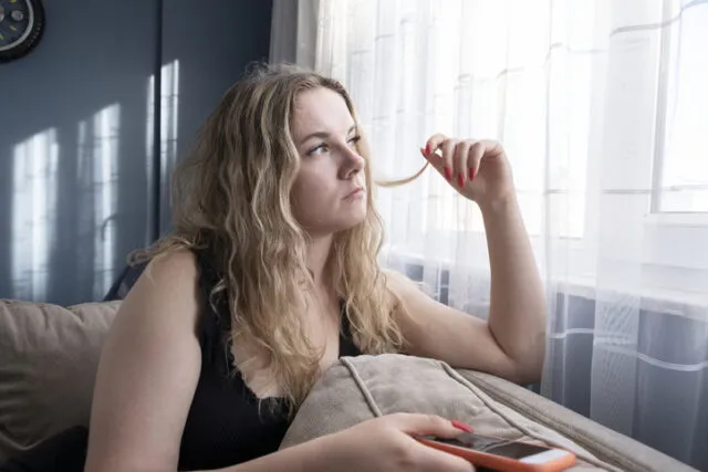 woman holding phone looking out window